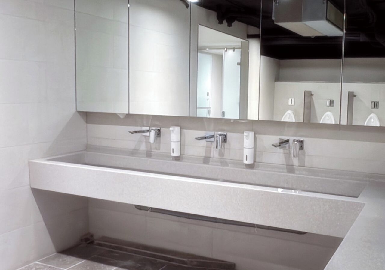 A modern bathroom with a large sink, multiple faucets, and a mirror above.
