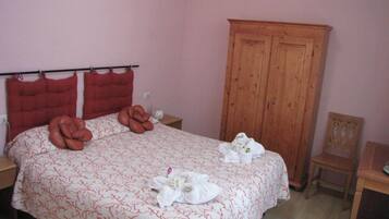 A neatly made bed with towels and a red headboard. There is a wooden wardrobe and a small table with a chair.