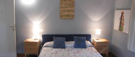 A neatly made bed with floral bedding, two bedside lamps, and a painting on the wall.