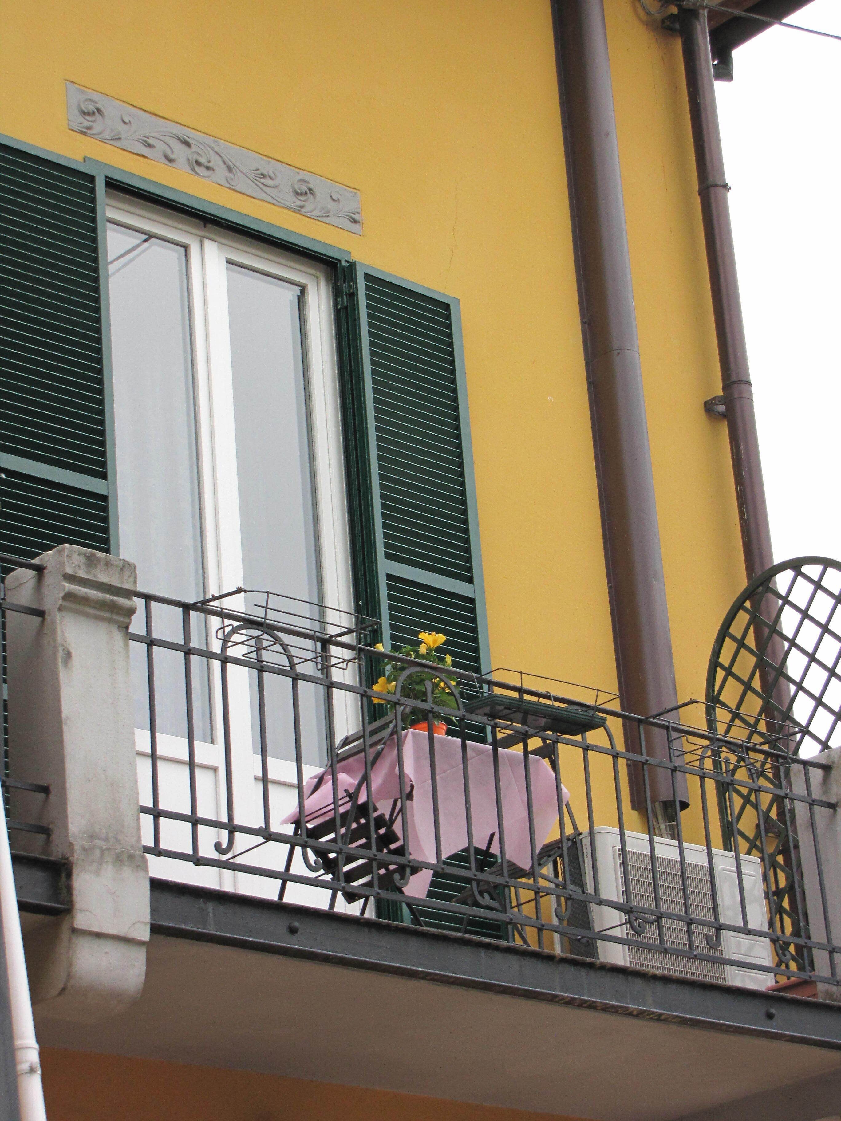 Un balcón con una mesa, sillas, una planta en maceta y una ventana con contraventanas.