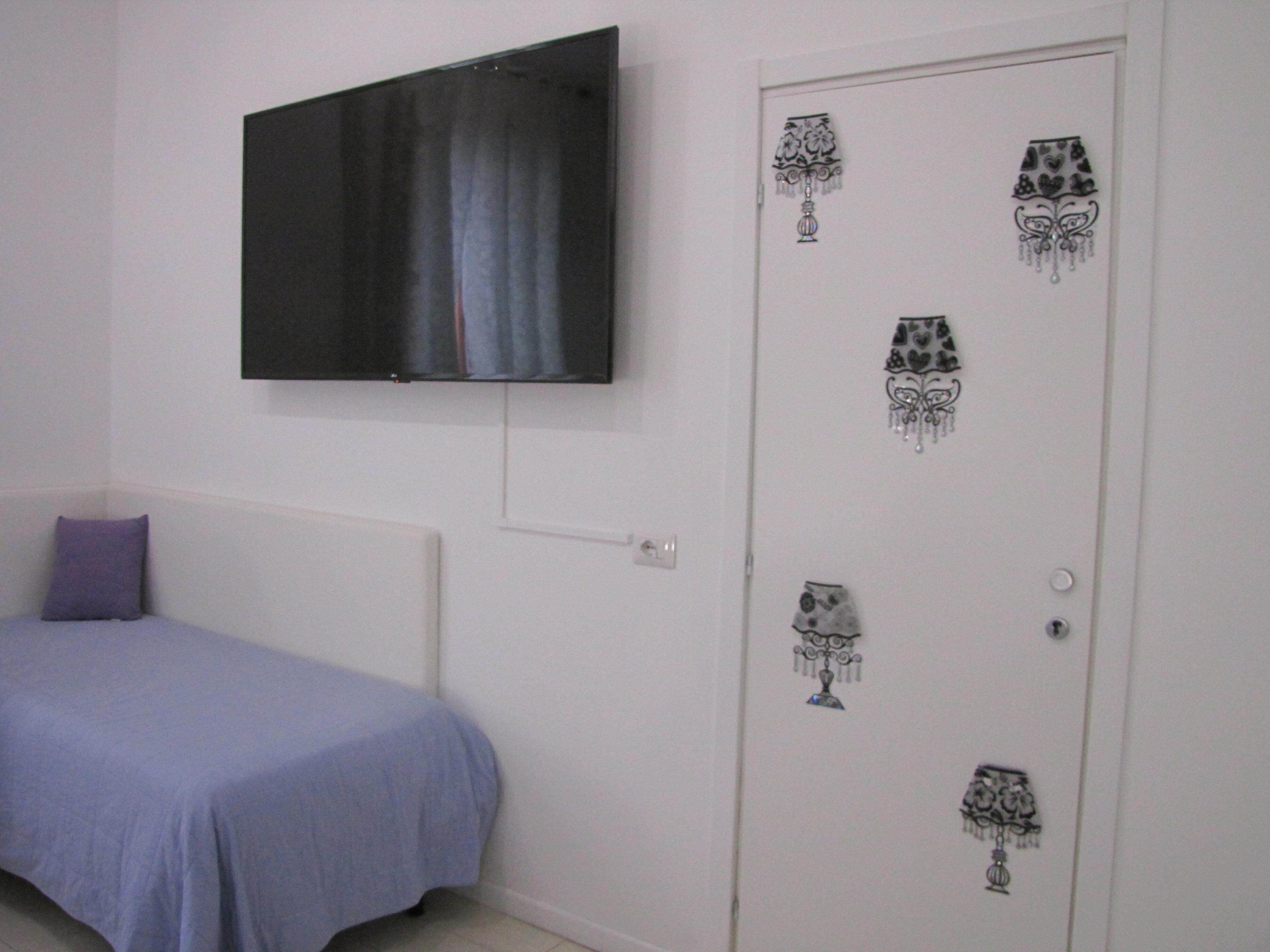 A bedroom with a bed, a TV mounted on the wall, and a door with decorative glass patterns.