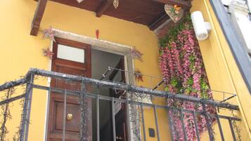 Um edifício amarelo com porta de madeira, portão de metal e flores cor-de-rosa na parede.