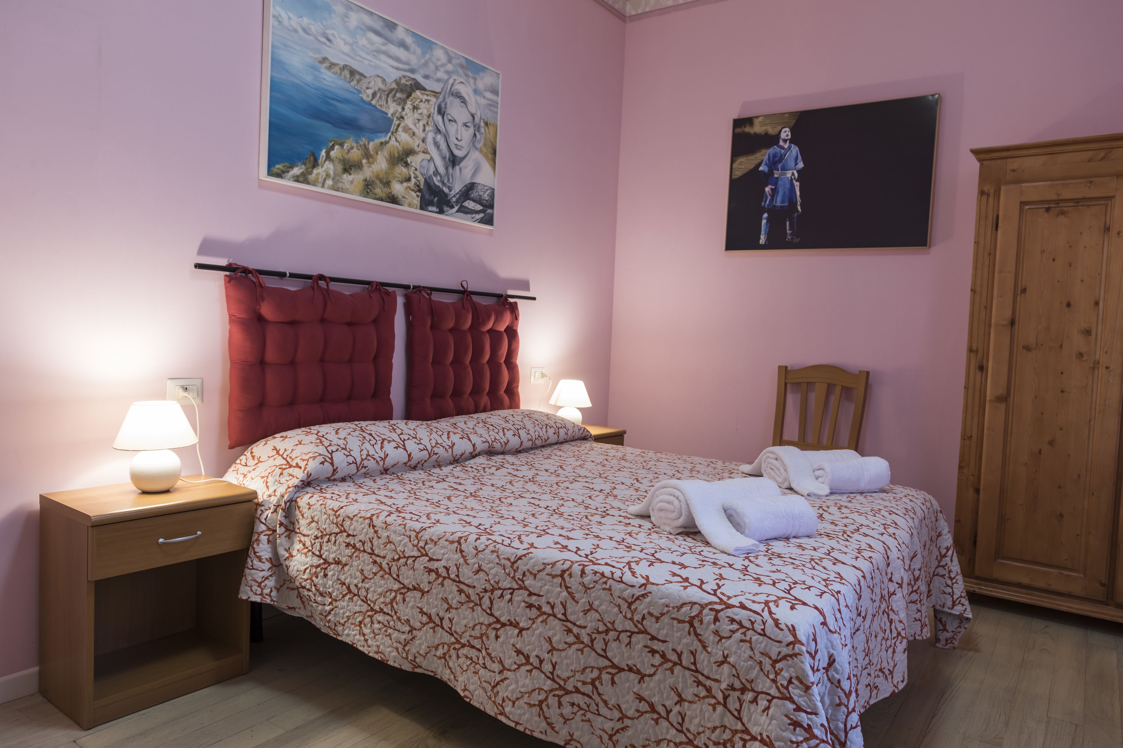 A bedroom with a bed, two bedside tables, a wooden wardrobe, and two wall-mounted paintings.