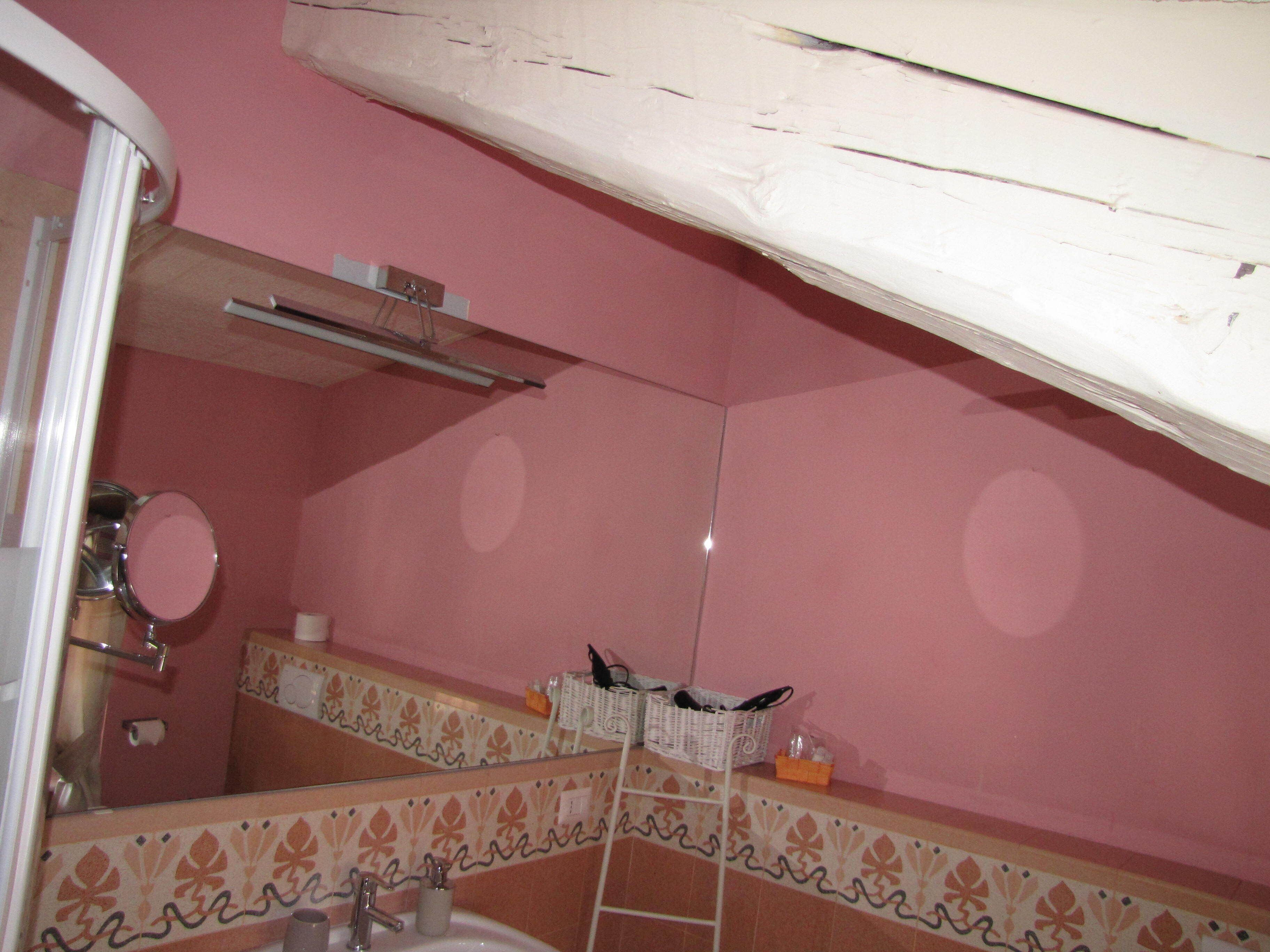Un baño con paredes rosadas, un lavabo blanco y un espejo. Hay un perchero sobre el lavabo y una repisa con artículos de aseo.