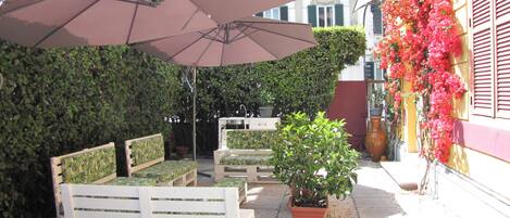 An outdoor seating area with a large umbrella, a white bench, and a potted plant.