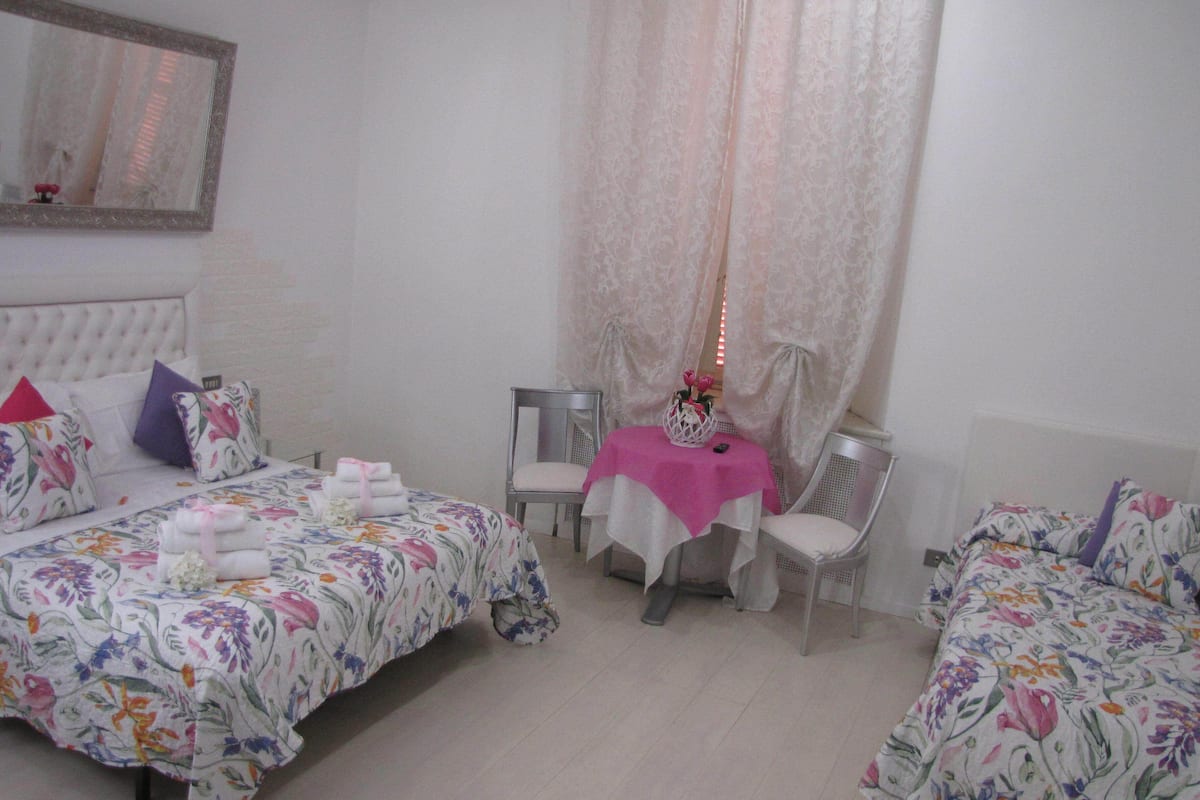 A hotel room with two beds, a small table with a pink tablecloth, and a chair.