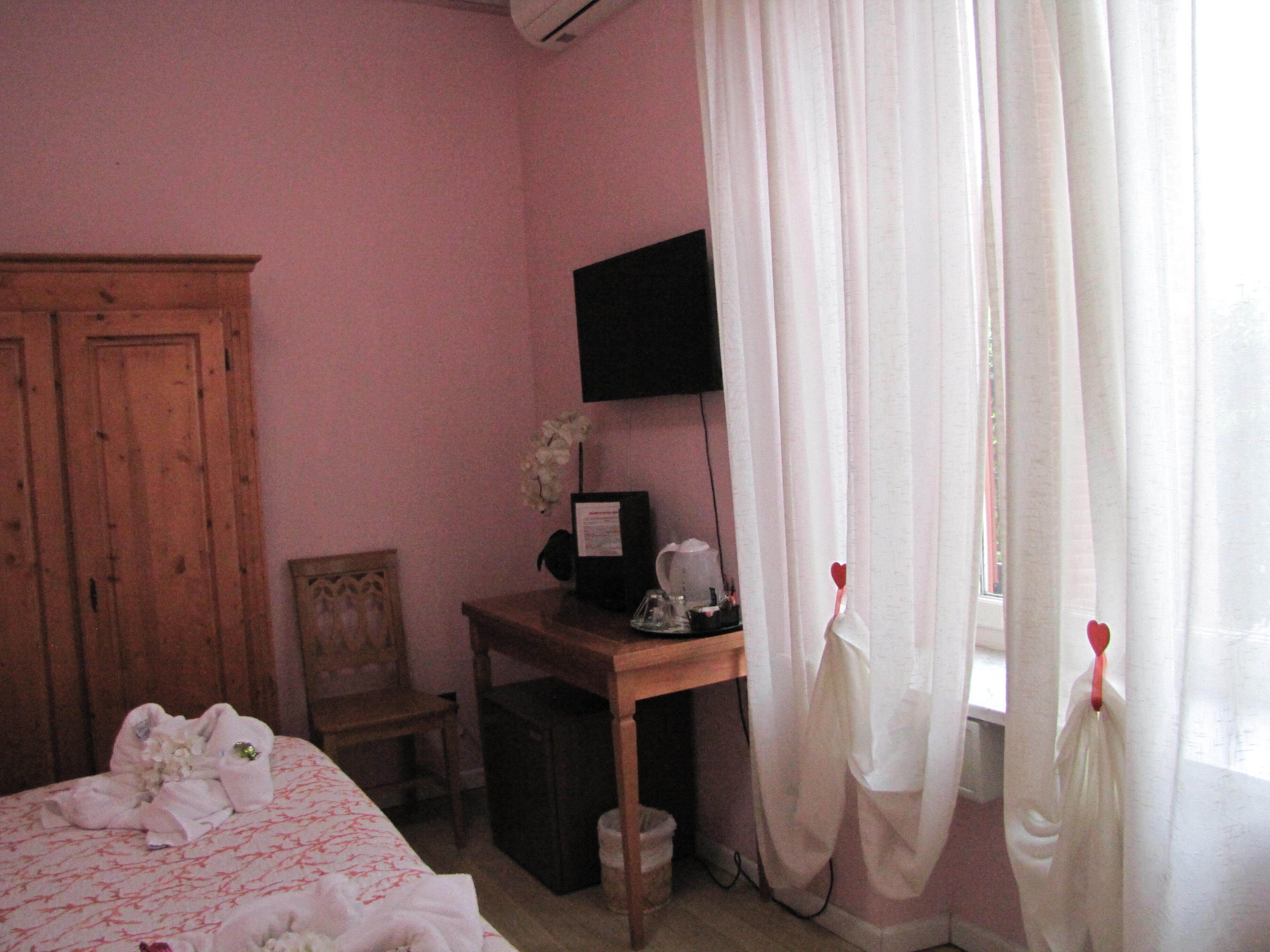 A bedroom with a bed, a desk, a chair, a TV, and a window with curtains.