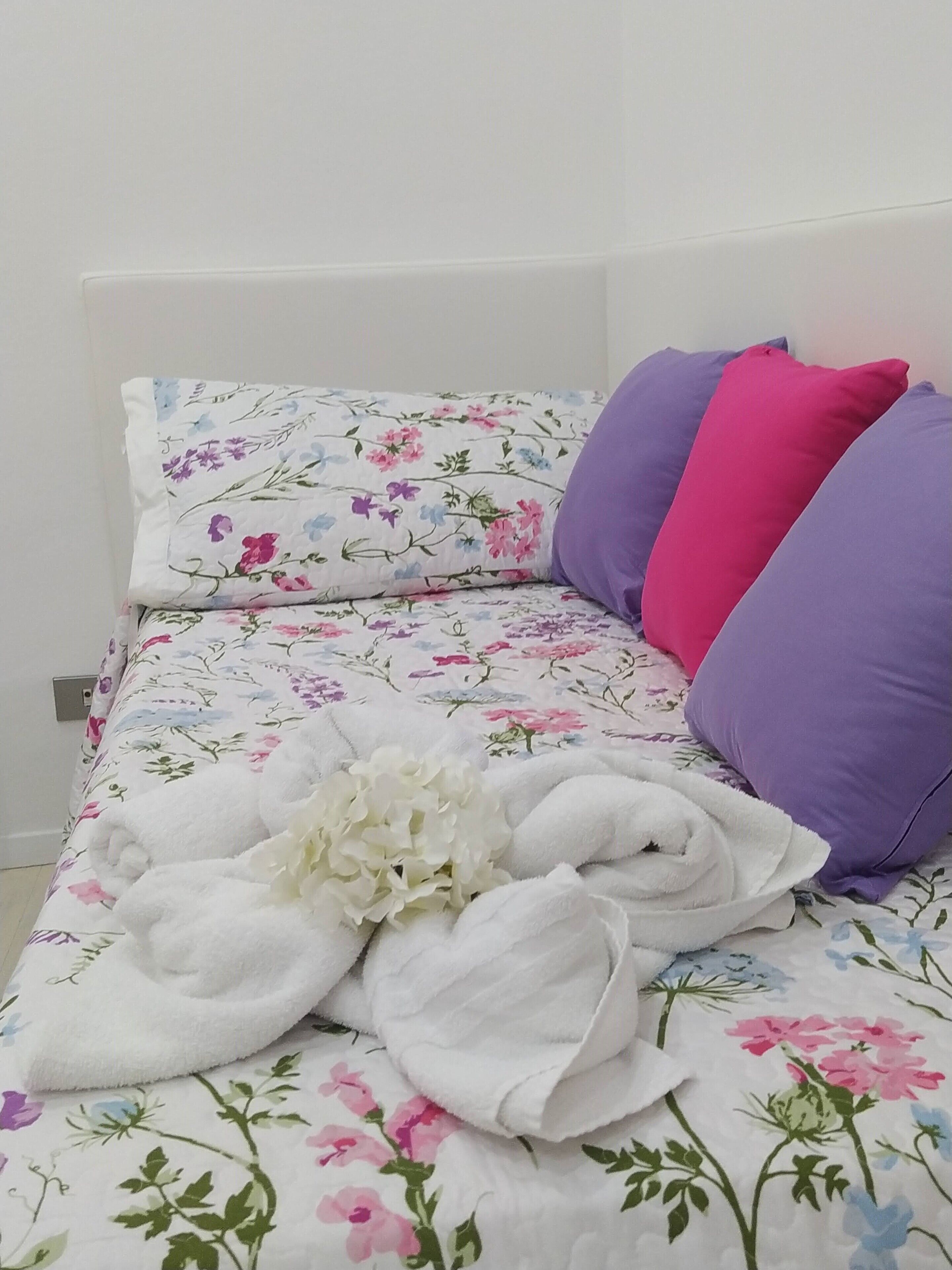 Una cama con ropa de cama floral, toallas blancas y almohadas moradas.