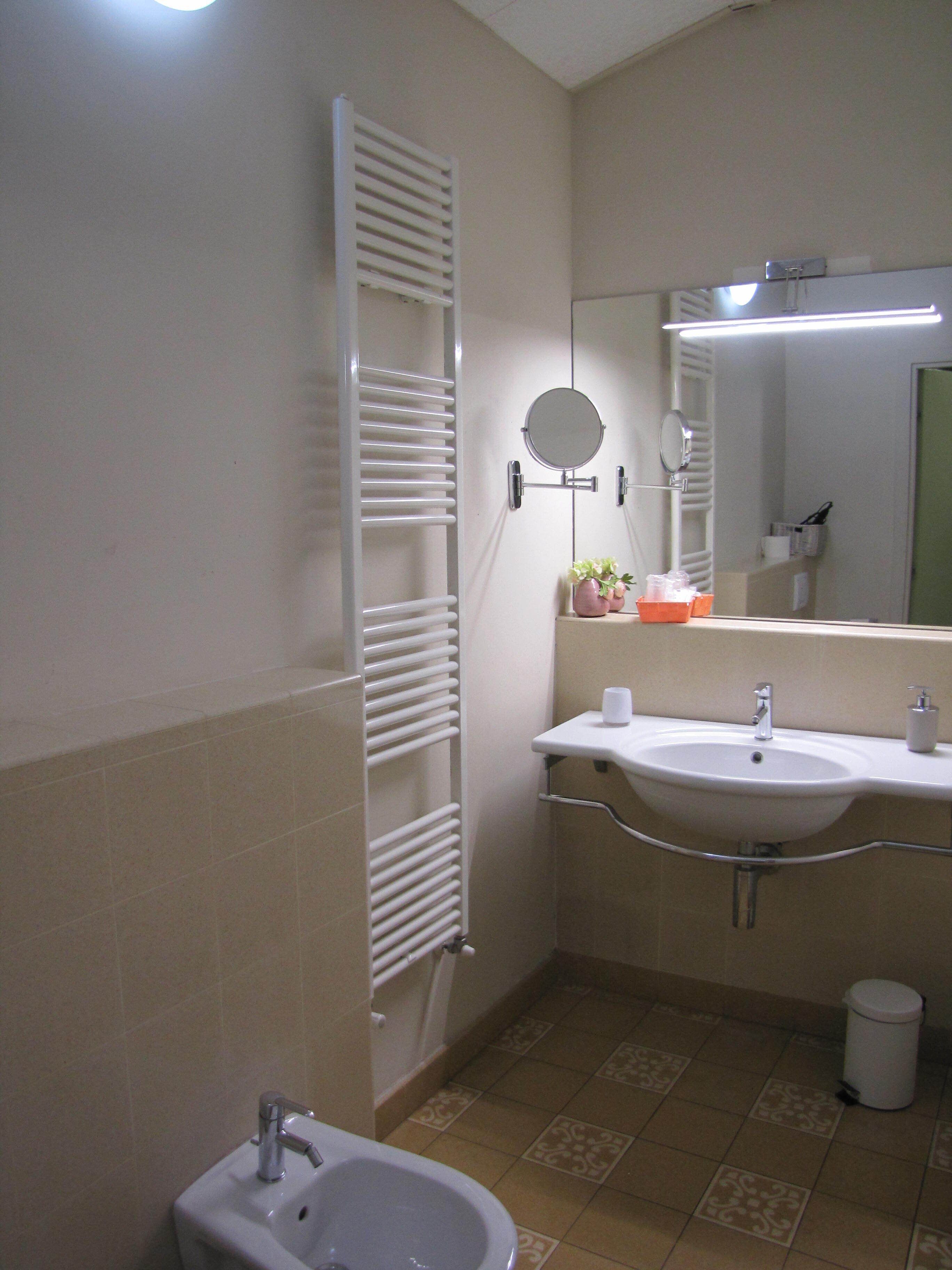 A bathroom with a white sink, a mirror, a towel rack, and a bidet.