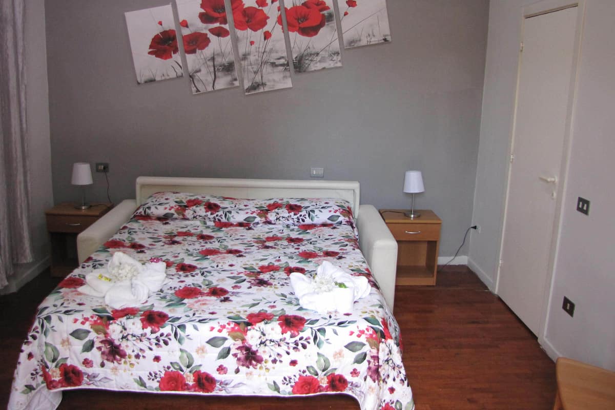 A bedroom with a floral bedspread, a white headboard, two bedside tables with lamps, and a door.