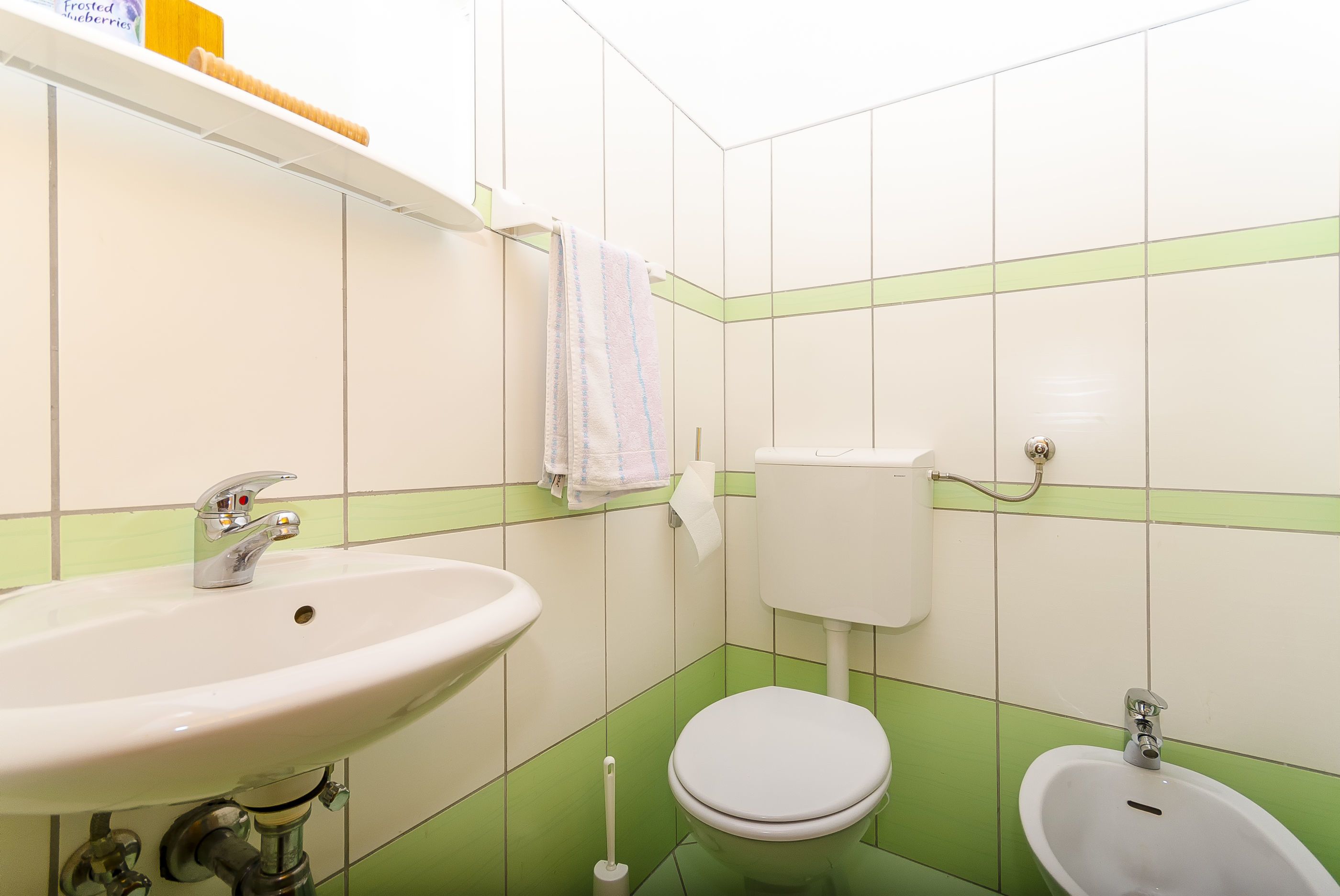 Un baño con lavabo, inodoro, bidé y paredes con azulejos verdes.