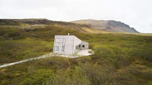 Une maison moderne dotée d’un toit plat et de grandes fenêtres, entourée d’un paysage naturel avec une montagne en arrière-plan.
