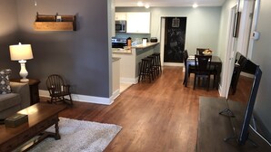 A modern living room with hardwood flooring, a sofa, a coffee table, and a TV stand. - Nana's Cottage 3 miles from downtown, pet friendly (Asheville)