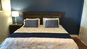 A neatly made bed with a dark headboard, a bedside lamp, and a blue wall. - Nana's Cottage 3 miles from downtown, pet friendly (Asheville)