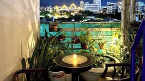 A balcony with potted plants, a table with a candle, and a cityscape view at night. - Cong Thuong Hotel (Da Nang)
