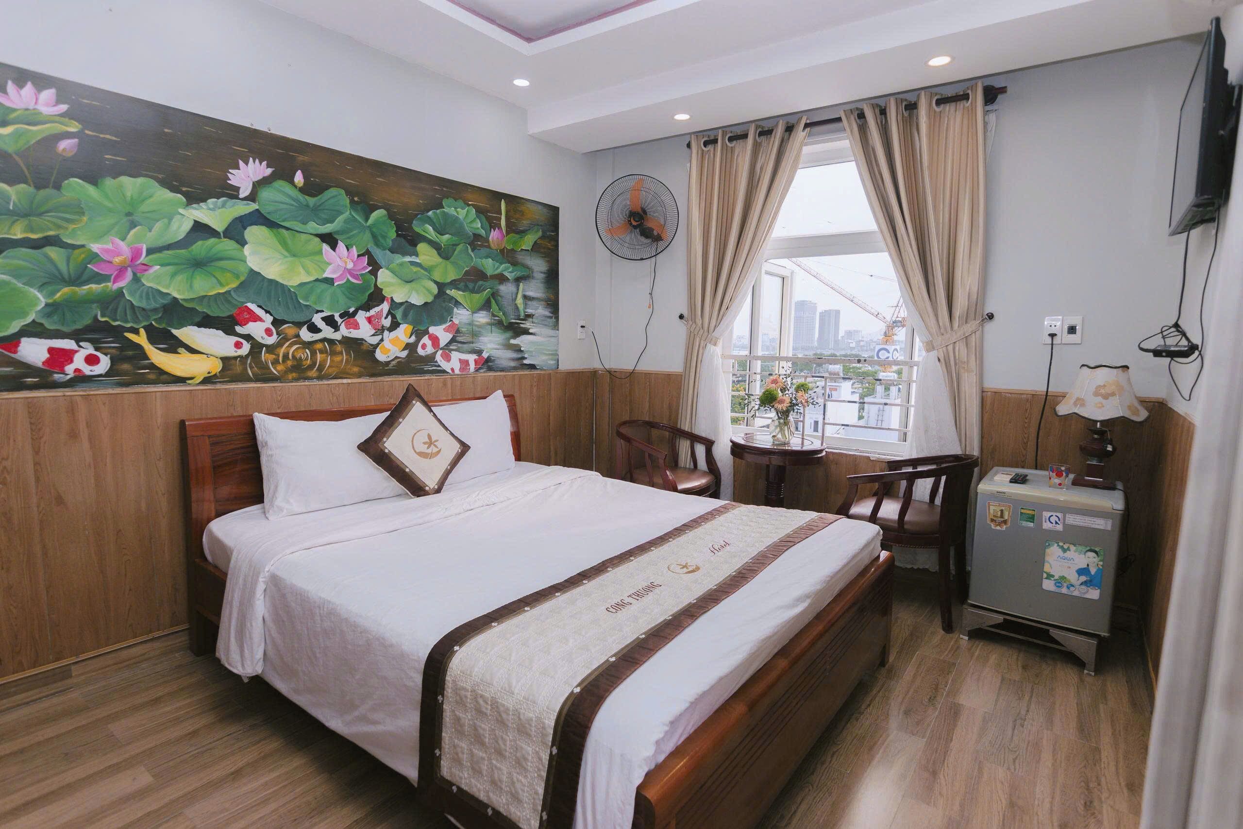 A hotel room with a bed, a desk, a chair, a fan, a TV, and a window with curtains.