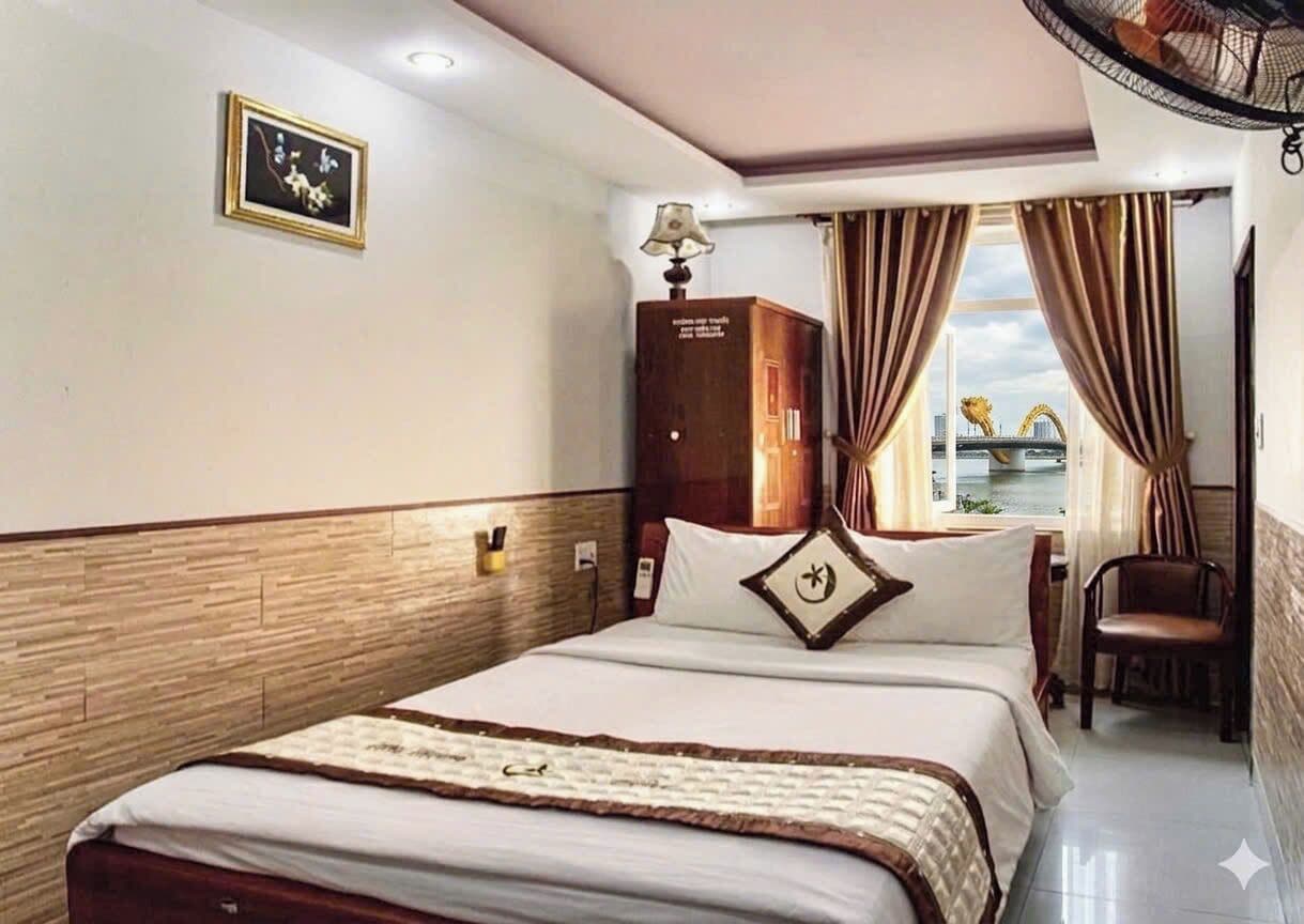 A hotel room with a bed, a desk, a chair, a lamp, a picture on the wall, and a window with curtains.