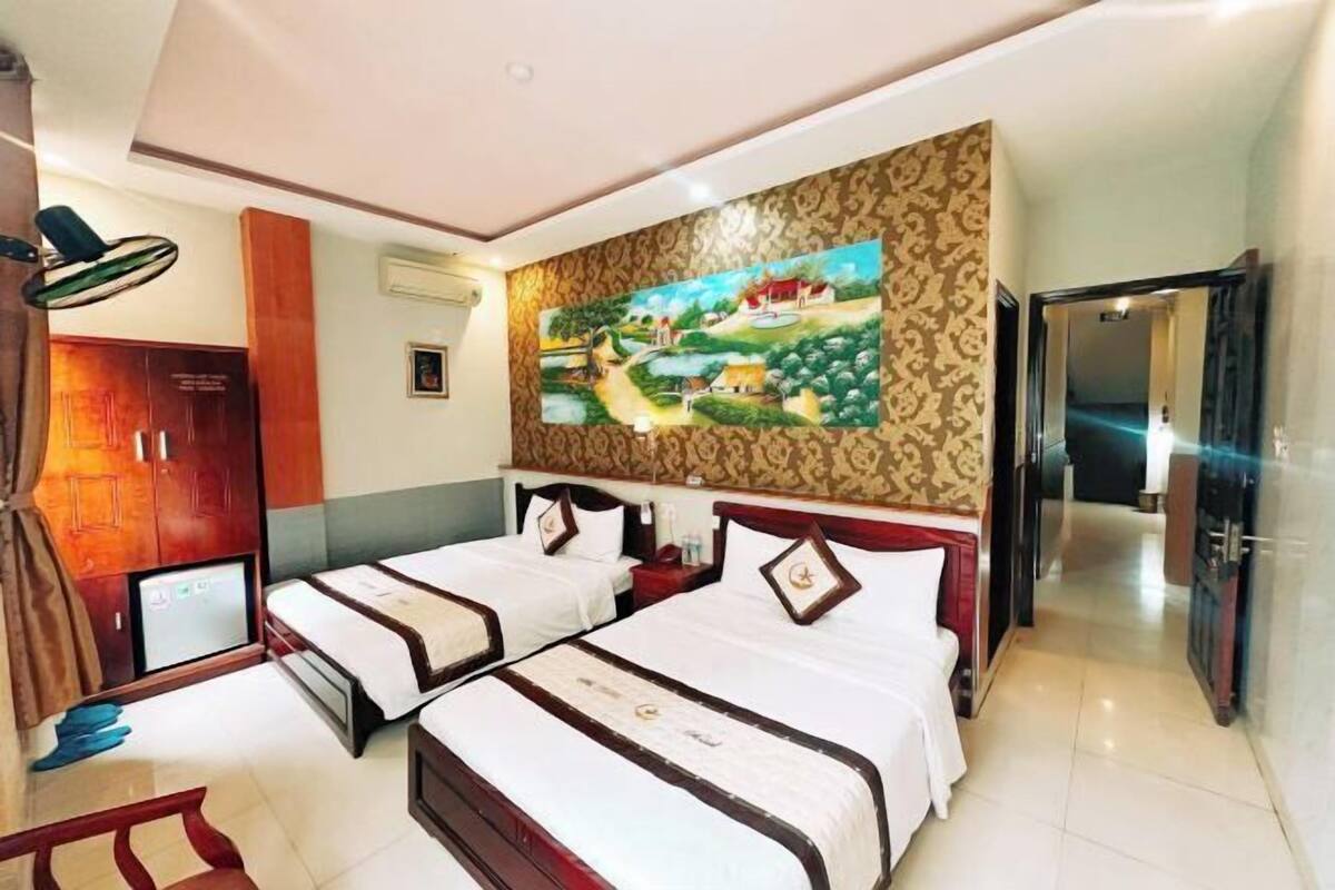 A hotel room with two beds, a painting on the wall, a desk, and a wardrobe.