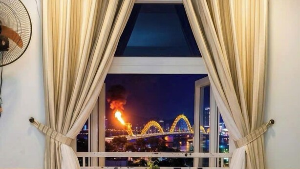 A hotel room with a bed, two chairs, a small table with a vase, and a window with curtains. - Cong Thuong Hotel (Da Nang)
