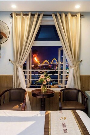 A hotel room with a bed, two chairs, a small table with a vase, and a window with curtains. - Cong Thuong Hotel (Da Nang)