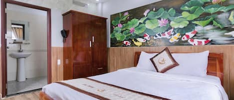 Habitación de hotel con cama, armario de madera, baño con lavamanos y un cuadro de nenúfares en la pared.