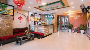 A hotel reception area with a reception desk, a sofa, a coffee table, and a wall with a clock and a sign. - Cong Thuong Hotel (Da Nang)