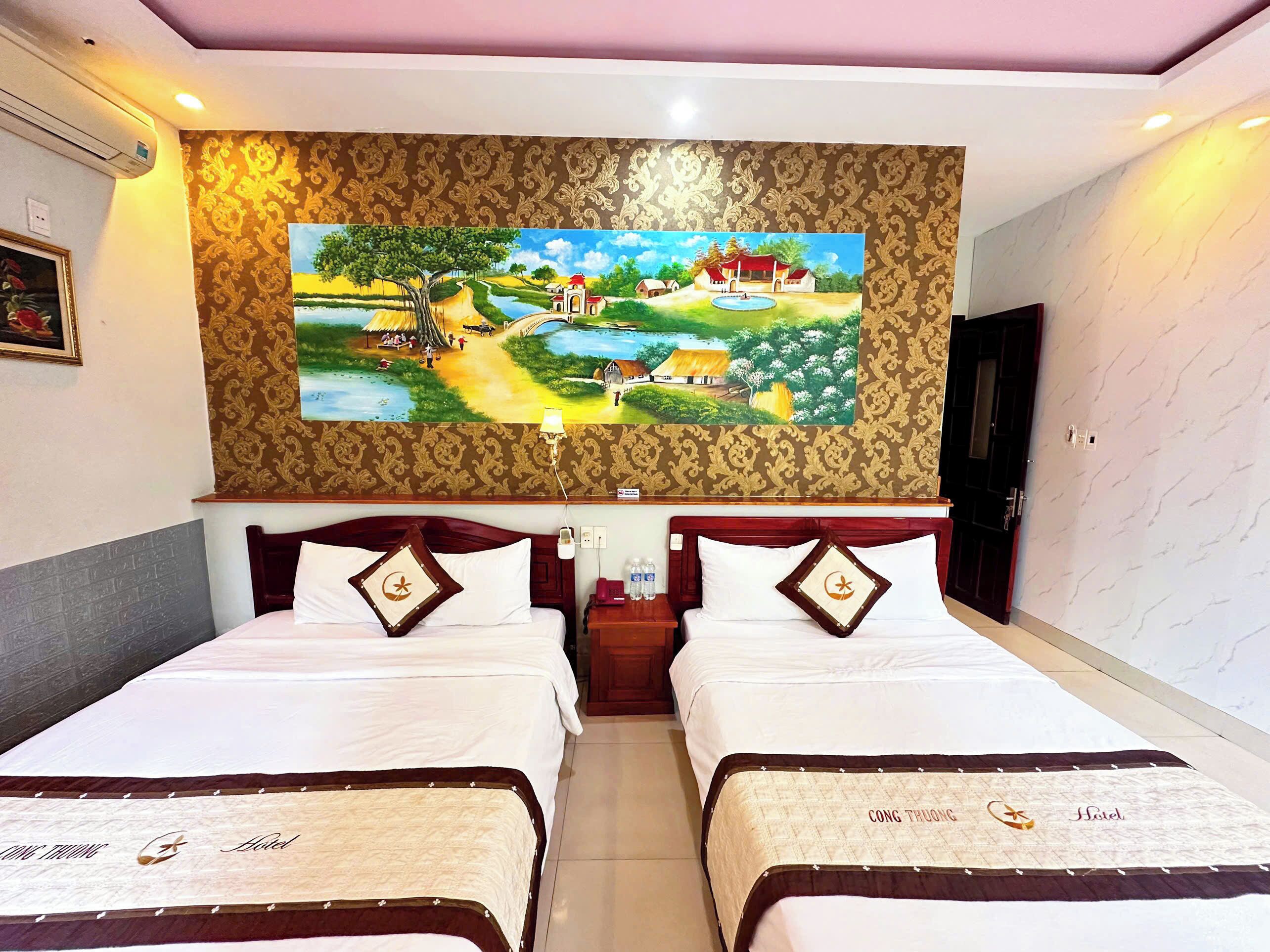 Una habitación de hotel con dos camas, un cuadro grande en la pared y una mesita de noche con una lámpara.