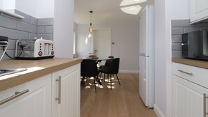 Een moderne keuken met witte kasten, een houten aanrecht, een broodrooster en een eethoek met stoelen.