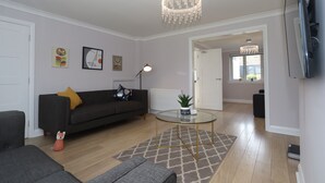 Een moderne woonkamer met een donkere bank, een glazen salontafel en een kroonluchter.