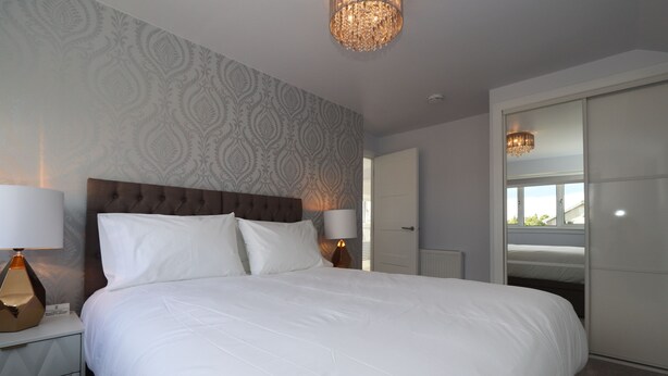 Een net opgemaakt bed met witte lakens, een gestuwd hoofdbord en twee bedlampjes.
