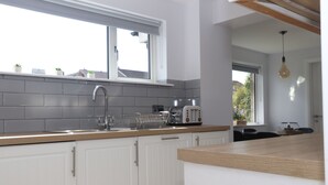 Een moderne keuken met witte kastjes, een grijze betegelde spatwand en een houten aanrechtblad.
