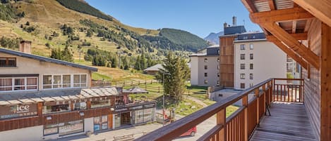 Bergzicht vanaf een houten balkon, met uitzicht op een stad, een restaurant en een skilift op de achtergrond.