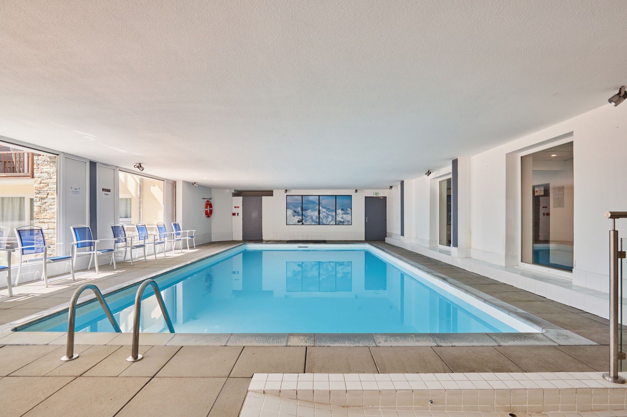 Una piscina interior con agua cristalina azul, rodeada de paredes blancas y suelo de baldosas.