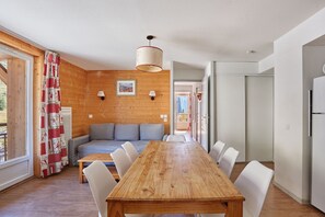 Ein Essbereich mit einem Holztisch und weißen Stühlen, einer Couch und einer Holzwand mit einem Bild.