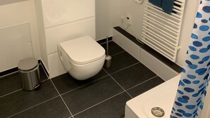 Un baño pequeño y moderno con tragaluz, inodoro, radiador y zona de ducha.