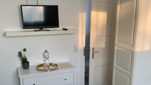 Un dormitorio con cama, televisor en un estante, cómoda con bandeja y puerta que da a un balcón.