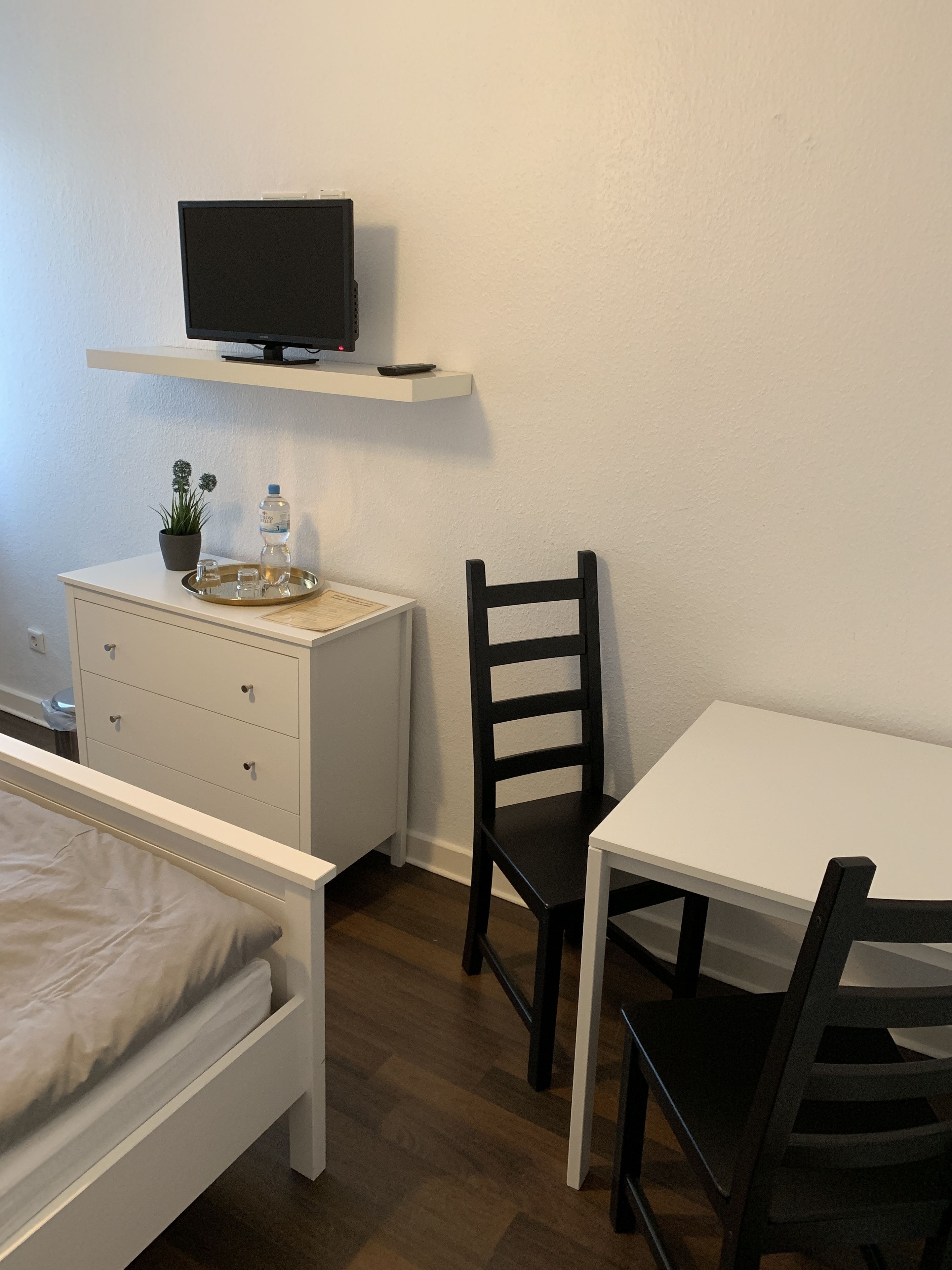 A bedroom with a bed, a bedside table with a TV, a chair, and a small table.