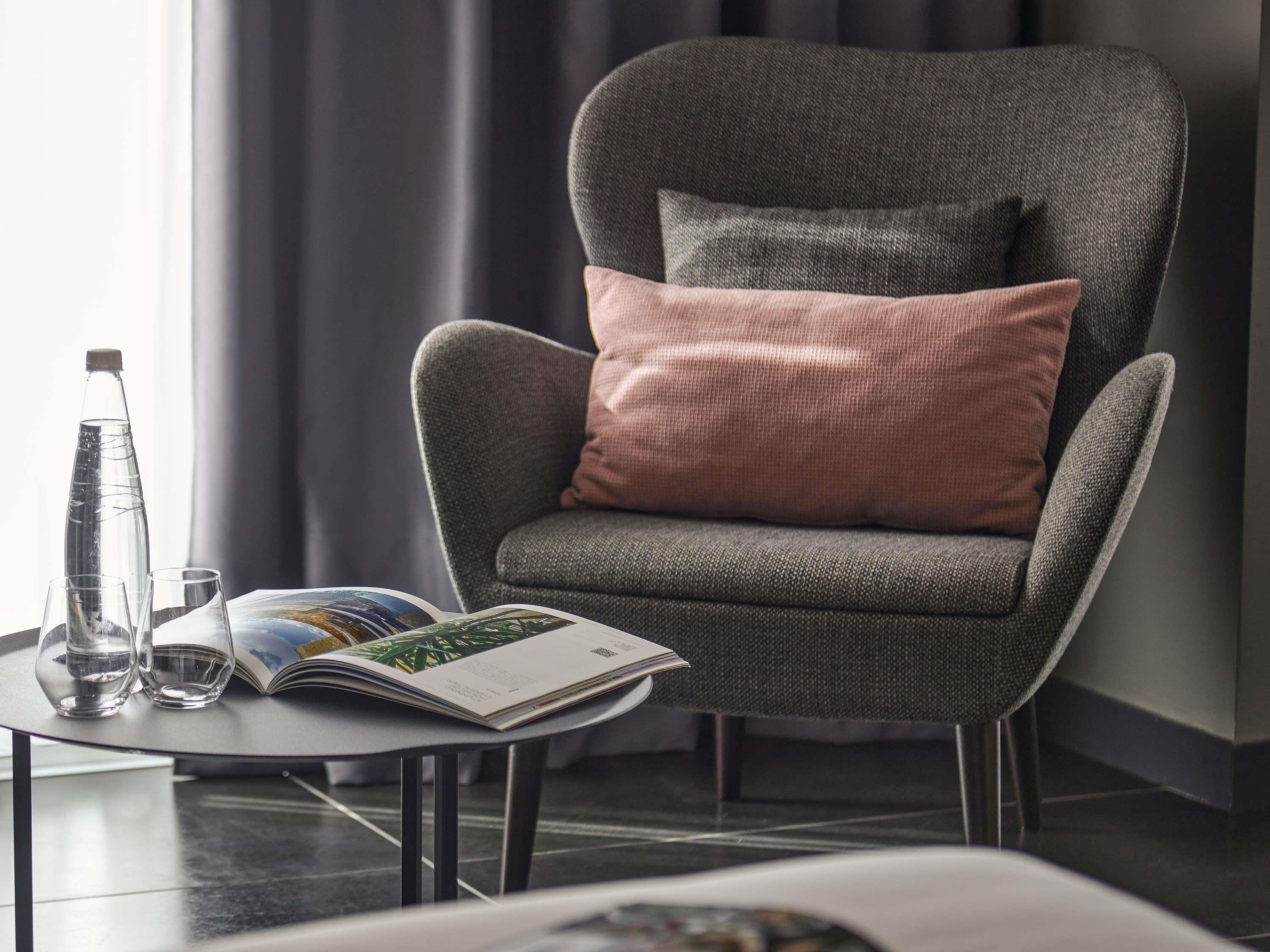 A modern armchair with a cushion, a glass bottle, and a magazine on a small table.