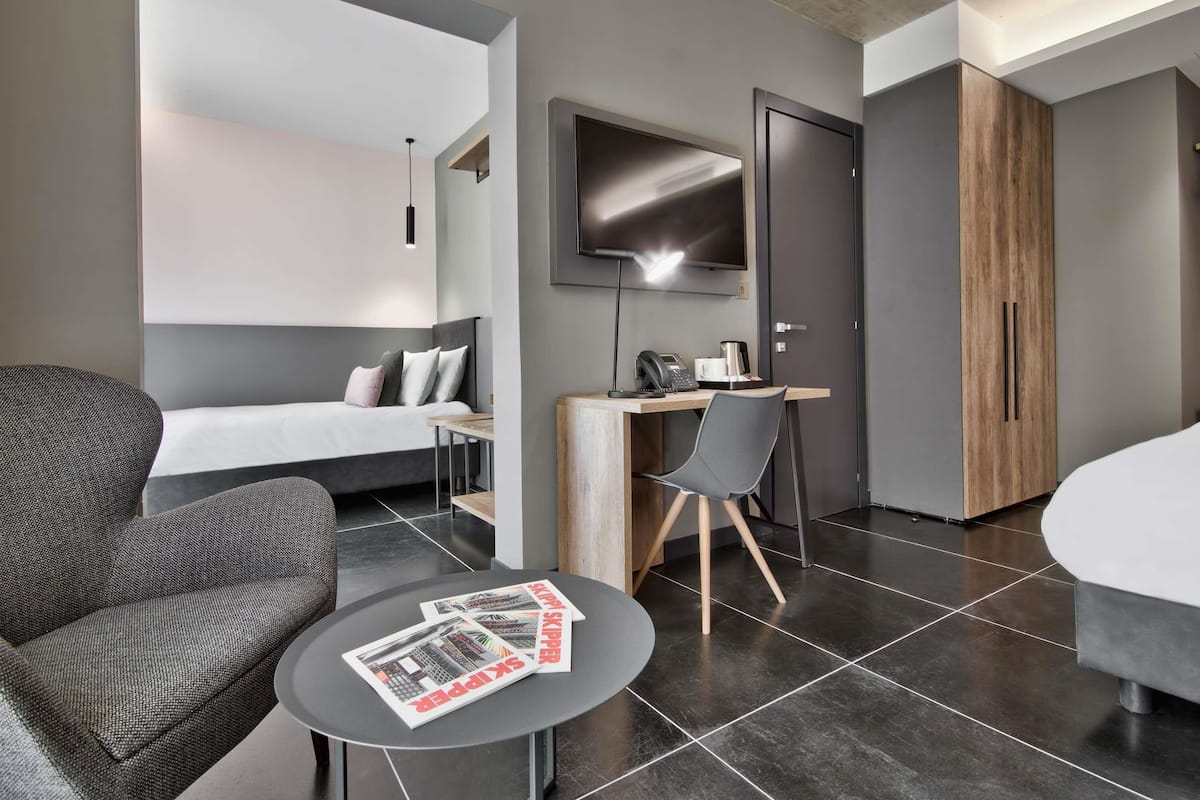 A modern hotel room with a bed, a desk, a chair, and a TV.