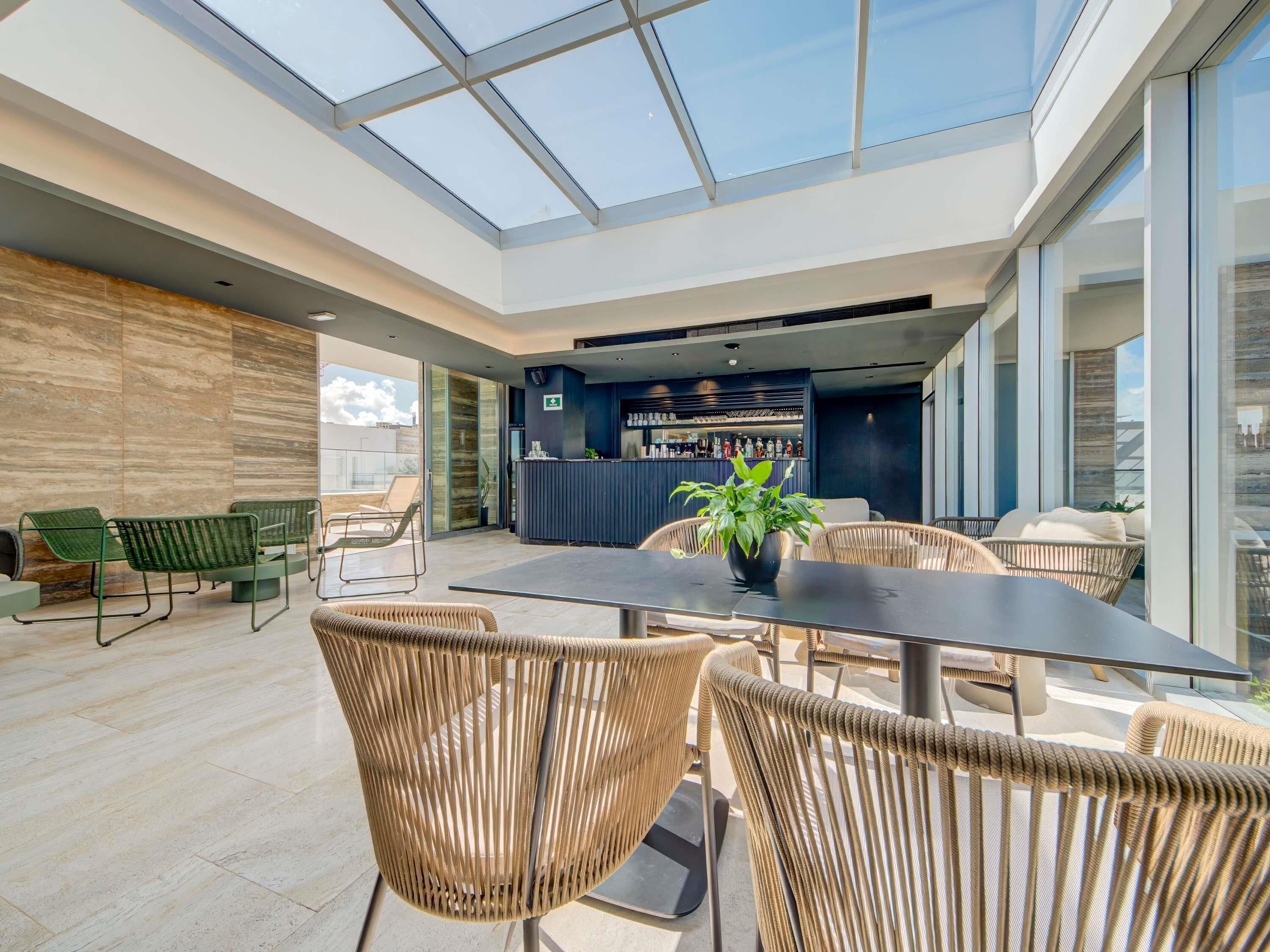 A modern indoor space with a glass ceiling, a bar area, and seating arrangements.