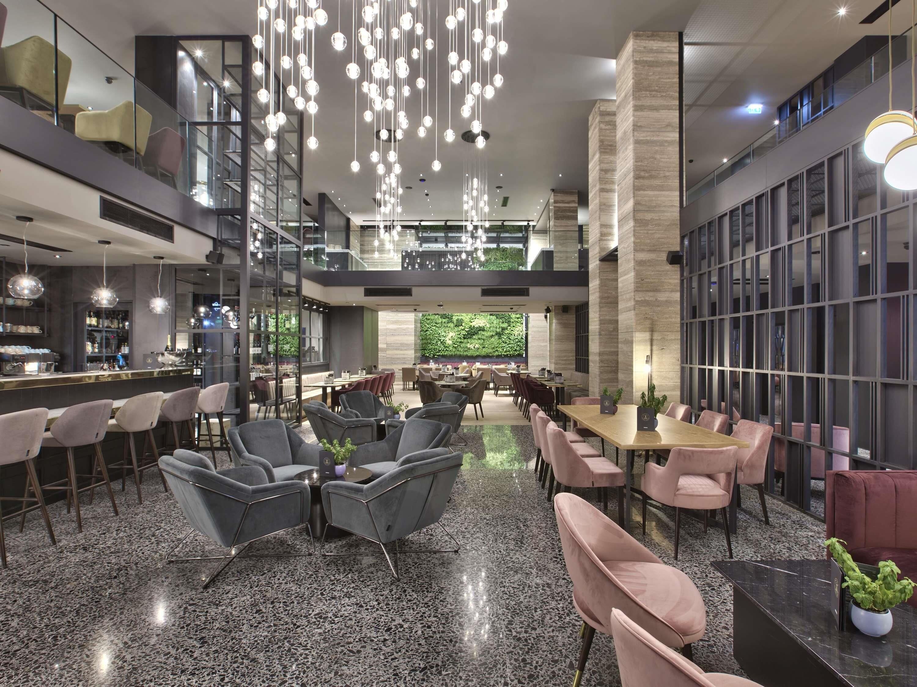 Un moderno vestíbulo de hotel con área de bar, arreglos de asientos y un amplio ventanal con vistas verdes.