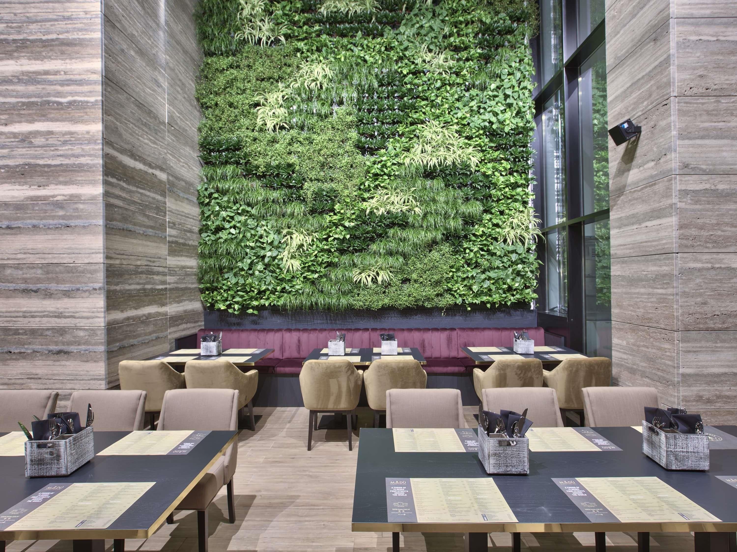 A restaurant with a green vertical garden wall, tables with menus, and cushioned chairs.