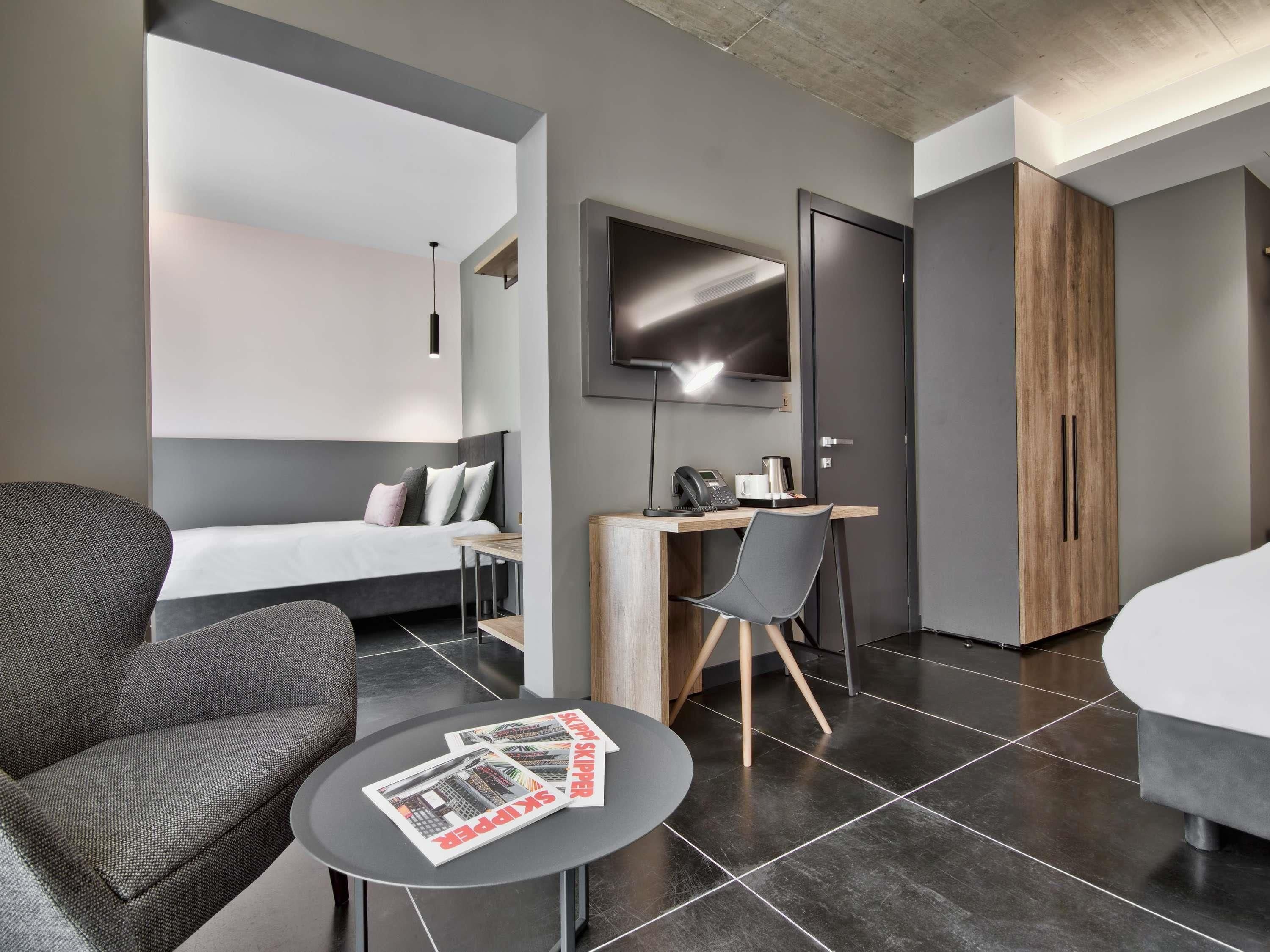 A modern hotel room with a bed, a desk, a chair, a TV, and a magazine on the table.