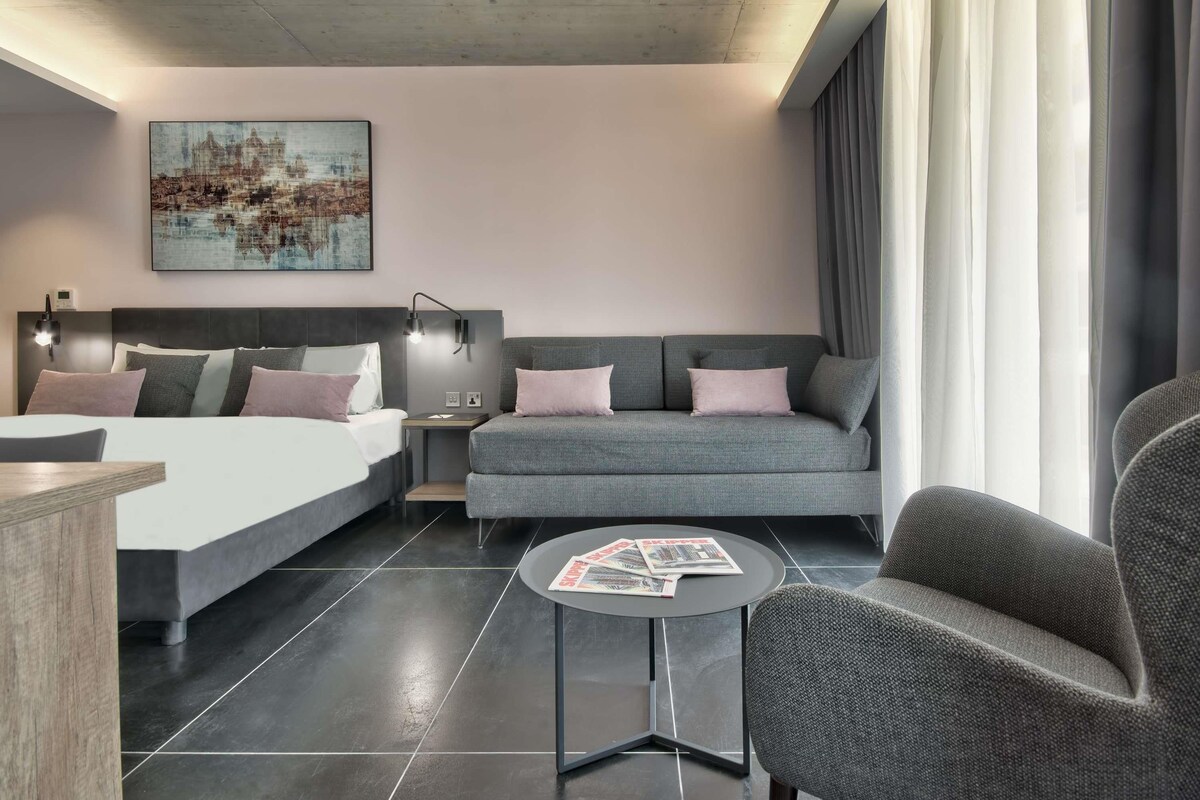 Una camera d'albergo moderna con un letto, una poltrona, un tavolino e un quadro appeso al muro.