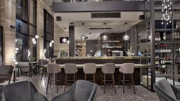 Zona de bar moderna con mostrador, taburetes y una estantería para vinos.