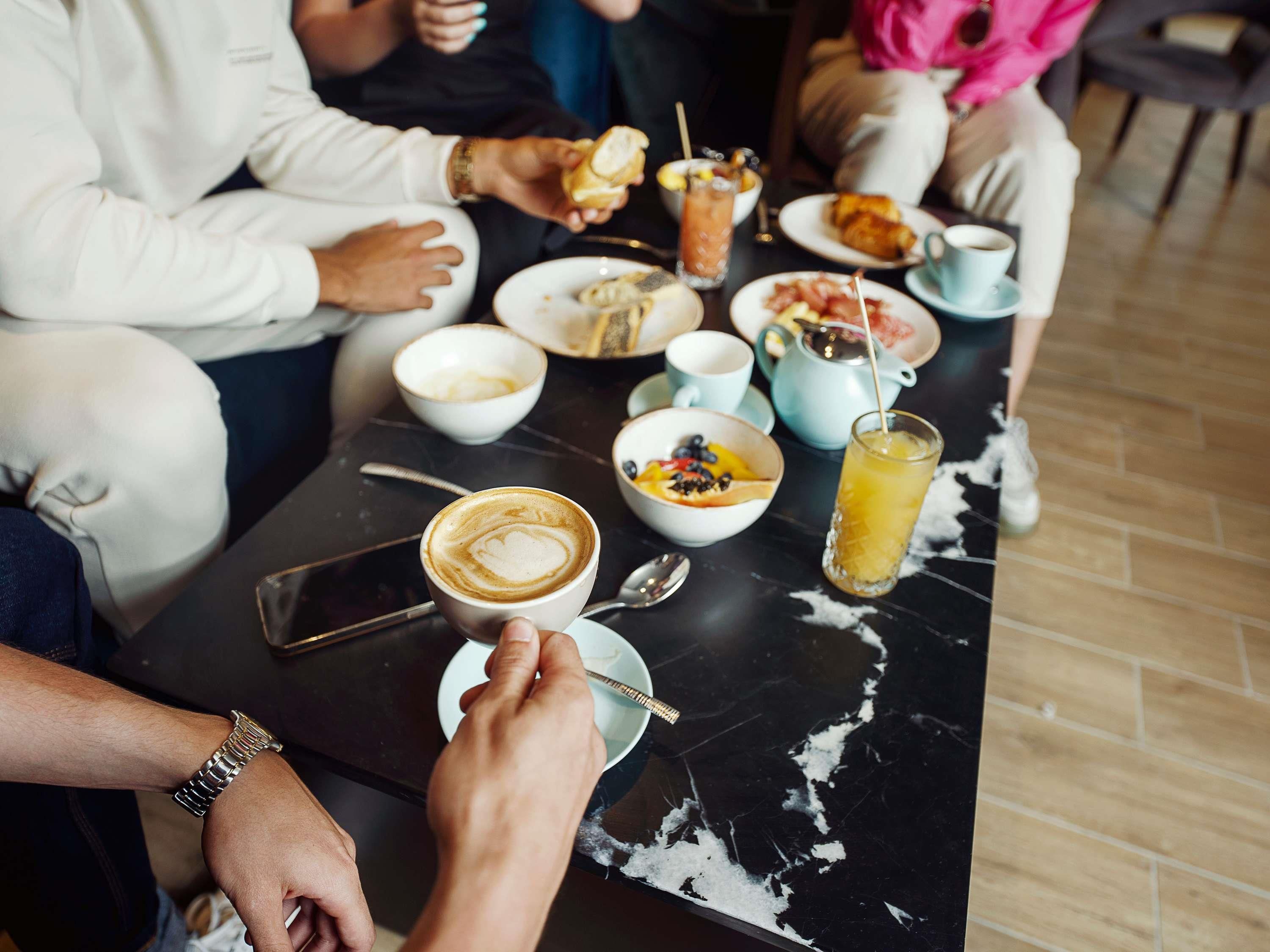A group of people seated around a table with various food items and drinks, including a cup of coffee and a glass of orange juice.