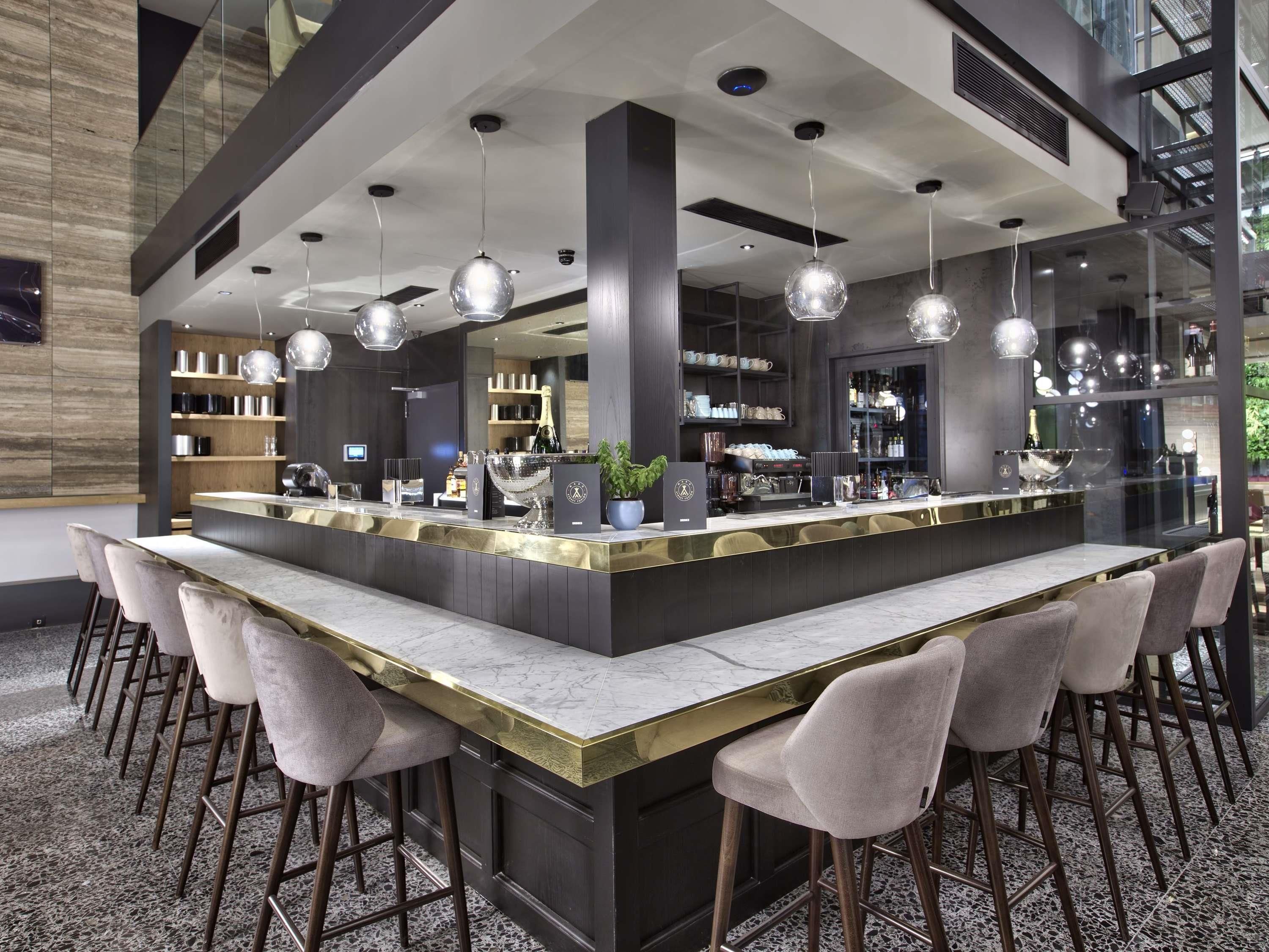 A modern bar area with a marble countertop, bar stools, and pendant lighting.