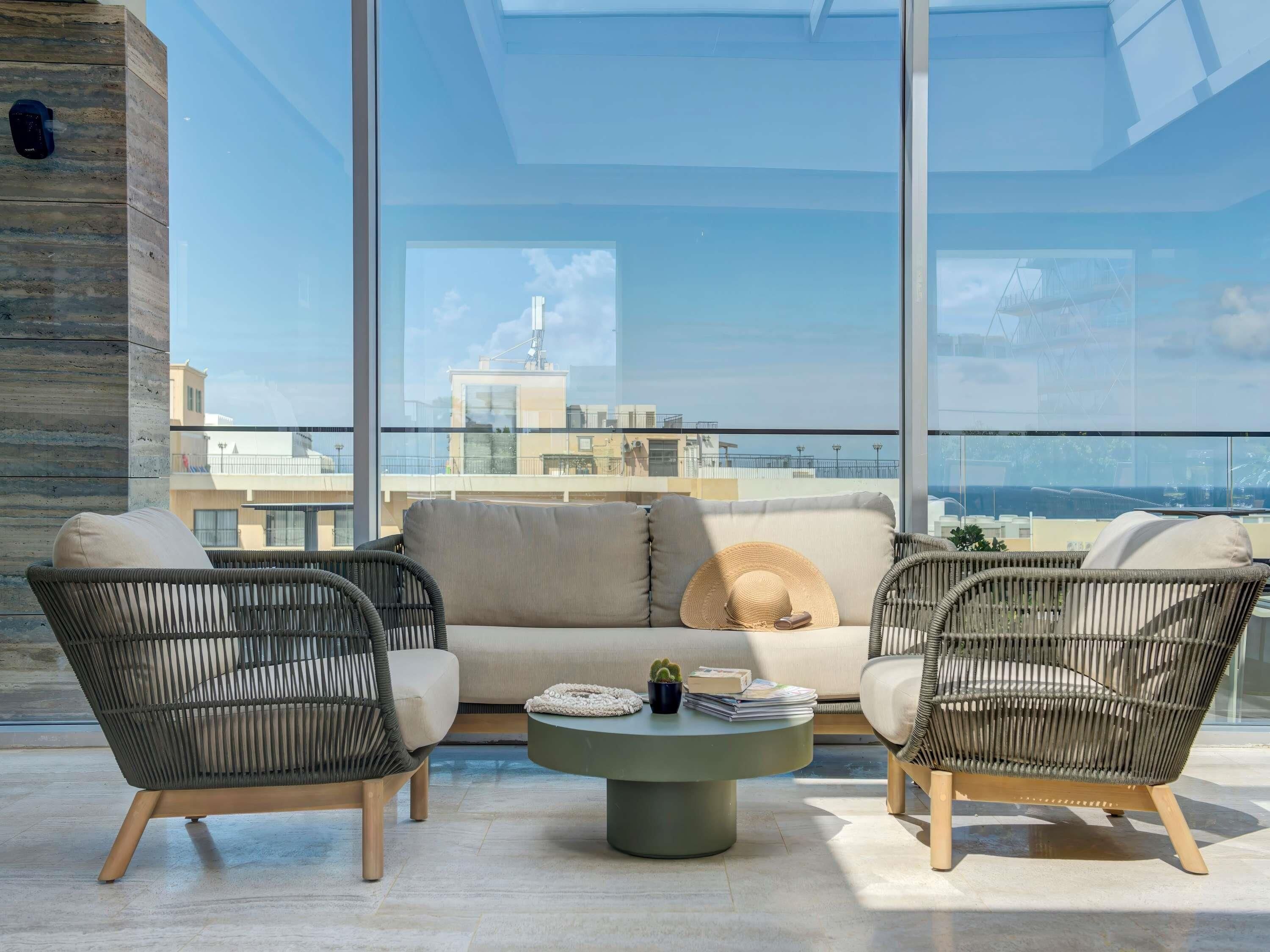 A modern lounge with wicker furniture, a round coffee table, and a view of a cityscape through large windows.