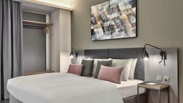 A modern hotel room with a large bed, two bedside tables, a wall-mounted abstract painting, and a ceiling light fixture.