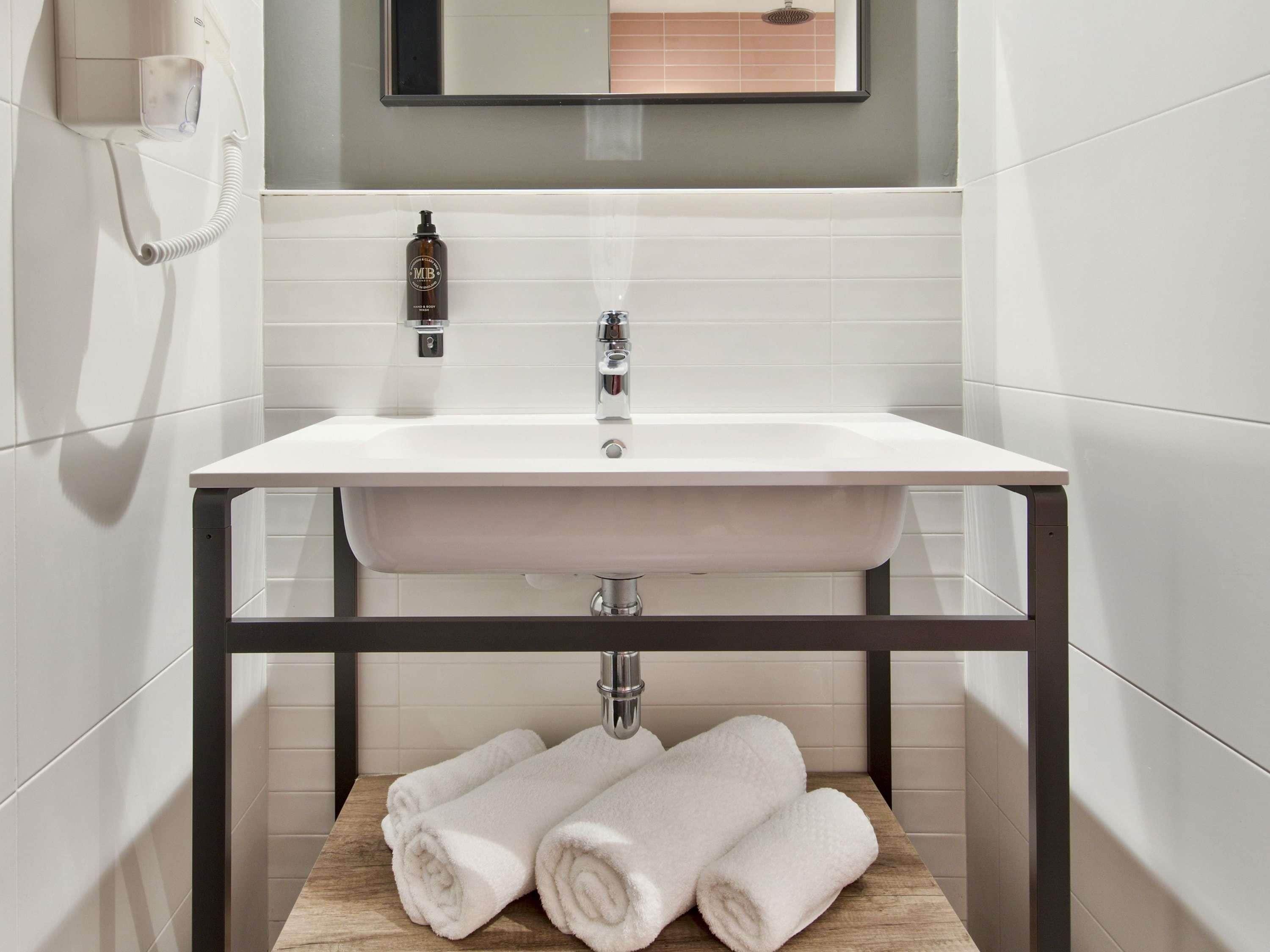 A bathroom with a white sink, a mirror above it, a towel rack with towels, and a phone on the wall.